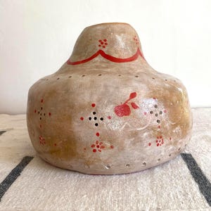 May include: A beige, gourd-shaped decorative vase with red painted accents. The vase features a wavy red line near the top and small red floral and dot patterns. Small holes are evenly spaced around the body of the vase.