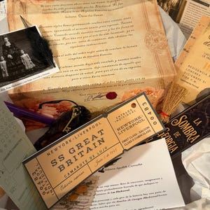 May include: A collection of vintage-style ephemera including a letter from Las Blackwood, a black and white photograph of a family, a New York-Liverpool SS Great Britain ticket, a small broom, a key, and a book titled La Sombra de Georgia.