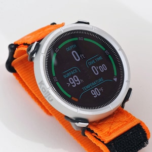 Peut inclure: Une montre de plongée argentée avec un bracelet orange et noir affiche la profondeur, le temps de plongée et la température. Le cadran indique "DEPTH 0 ft", "DIVE TIME 0'00" et "TEMPERATURE 90°F". La montre est marquée "Kalju".