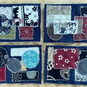 May include: Four rectangular fabric patches featuring dark blue denim bases layered with various textile scraps. The patches display assorted patterns including floral, polka dot, and geometric designs, with one patch featuring a small illustration of cats.