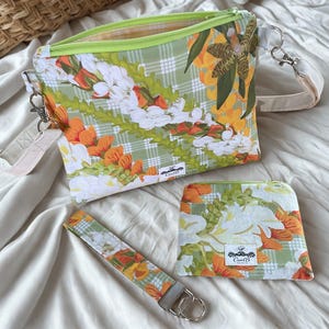 May include: A crossbody bag with a lime green zipper, a matching small pouch, and a wristlet strap. The fabric features a green plaid background with orange and white floral lei patterns. Each item has a white label with the text CarolB.