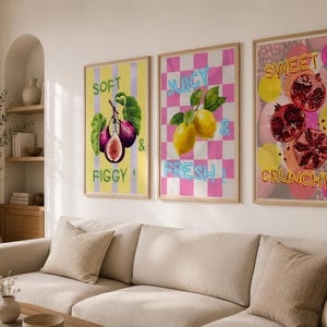 Puede incluir: Tres impresiones artísticas enmarcadas con ilustraciones de frutas cuelgan sobre un sofá. Las impresiones presentan higos, limones y granadas con el texto "Soft & Figgy!", "Juicy & Fresh!" y "Sweet & Crunchy!"