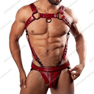 May include: A red leather harness with suspenders and a jockstrap. The harness features metal rings and rivets. The product is designed with adjustable straps and a contoured fit. The image is of a person wearing the harness.