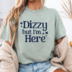 Könnte beinhalten: Hellgrünes T-Shirt mit dem marineblauen Text "Dizzy but I'm Here" und Sternen. Das T-Shirt hat einen lässigen Stil und ist einfarbig.