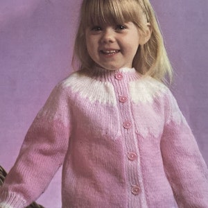 May include: A pink knitted cardigan with a white trim and button closure. The cardigan has a fair isle pattern on the front and sleeves.