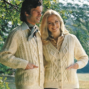 Könnte beinhalten: Zwei cremefarbene Strickjacken mit Zopfmuster, Knöpfen und Taschen. Die Strickjacken sind aus einem weichen, strukturierten Garn gefertigt.