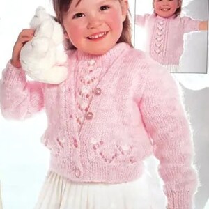 May include: A pink knitted cardigan with a button closure and a delicate heart pattern. The cardigan has long sleeves and a slightly cropped length.