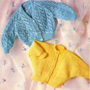 May include: Two knitted baby cardigans, one blue with a lacy pattern and one yellow with a cable pattern.
