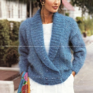 May include: A blue fuzzy cardigan with a shawl collar and two buttons. The cardigan is worn over a white shirt and white pants. A colorful scarf is tucked into the waistband of the pants.