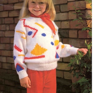 May include: A white knitted jumper with a geometric pattern in red, yellow, blue, and orange. The jumper has a round neckline and long sleeves.