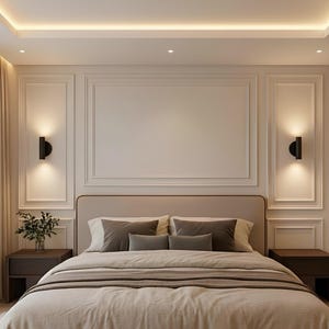 May include: A bedroom featuring a beige upholstered bed with grey pillows and a matching bedspread. The room has a neutral colour scheme, decorative wall panels, sconce lighting, and dark wood bedside tables.