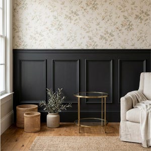 Op de afbeelding: Een kamer met bloemenbehang, zwarte lambrisering en een gouden bijzettafel met een glazen blad. Gevlochten manden en een plant in een pot staan op de houten vloer. Een beige fauteuil met een deken staat in de hoek.