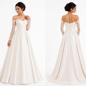 May include: An off-the-shoulder floor-length gown in ivory satin featuring long, sheer lace sleeves and a sweetheart neckline. The bodice is fitted with a structured waistline, transitioning into a full, pleated skirt with a train.