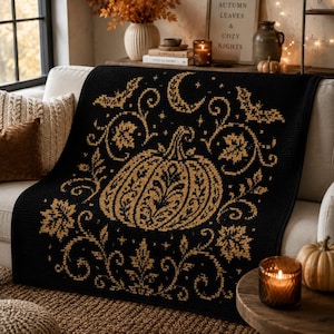 May include: A black throw blanket featuring a gold-colored embroidered design of a central pumpkin surrounded by swirling vines, autumn leaves, bats, and a crescent moon. The intricate pattern is centered on the fabric with a textured finish.