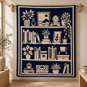 May include: A dark navy blue and cream crochet blanket featuring a bookshelf design. The pattern displays rows of books, potted plants, a framed picture, a clock, and a mug. The rectangular textile has a thick cream border and a pixelated aesthetic.