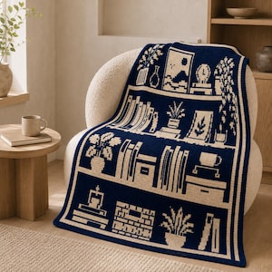 May include: A dark blue and cream crochet blanket featuring a repeating pattern of bookshelves filled with books, potted plants, a clock, a framed picture, and a mug. The design is rendered in a pixelated style with clean horizontal lines.