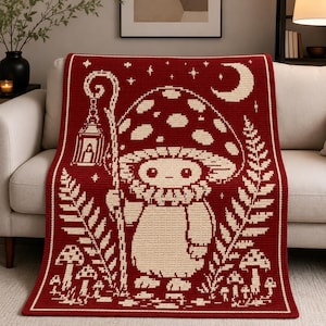 May include: A rectangular crochet blanket featuring a deep red background with a cream-colored pixelated design. The pattern depicts a central mushroom-headed creature holding a lantern, surrounded by ferns, smaller mushrooms, and a crescent moon.