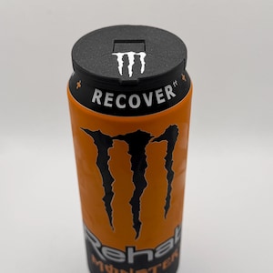 Könnte beinhalten: Eine orangefarbene Monster Rehab Energy-Drink-Dose mit Tee-Geschmack und einem schwarzen Deckel. Die Dose zeigt das Monster-Logo und das Wort "RECOVER" in Weiß. Die Dose hat schwarze Krallen und die Worte "Rehab Monster Tea + Peach".