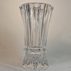May include: A clear, faceted crystal vase with a flared top and a decorative base. The vase features vertical, linear cuts that create a textured surface. The vase is approximately 10 inches tall.