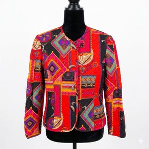 Könnte beinhalten: Eine langärmelige, gesteppte Jacke mit einem lebendigen Patchwork-Muster in den Farben Rot, Schwarz, Violett, Orange und Türkis. Die Jacke hat einen Rundhalsausschnitt und wird vorne mit drei silberfarbenen Knebelverschlüssen geschlossen.