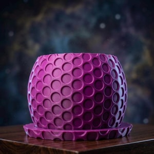 May include: A magenta-colored, spherical planter with a textured pattern of recessed circles. The planter sits on a matching saucer. The design is reminiscent of a golf ball. The background is a blurred image of a galaxy.