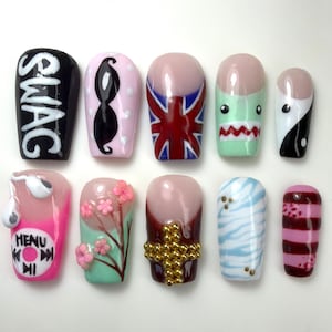 May include: A collection of ten artificial nails with various designs. The designs include the word "SWAG", a black mustache on a pink background, a Union Jack, a shark, a yin-yang symbol, a music player, cherry blossoms, a gold cross, blue zebra stripes, and red and pink stripes.