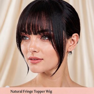 Może przedstawiać: Kobieta z ciemnymi włosami w peruce z grzywką. Peruka ma naturalny wygląd z grzywką oprawiającą twarz. Tekst "Natural Fringe Topper Wig" znajduje się na dole obrazu.