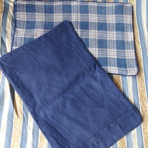 May include: Two pillowcases, one with a blue and white plaid pattern and the other a solid blue color. Both pillowcases have a dark blue border.