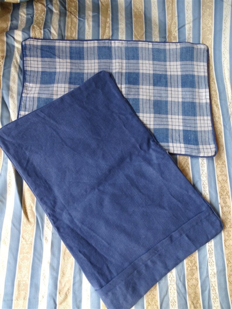 May include: Two pillowcases, one with a blue and white plaid pattern and the other a solid blue color. Both pillowcases have a dark blue border.