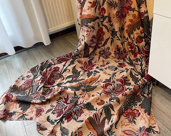 May include: A beige fabric with a floral pattern in shades of red, green, and orange. The fabric is folded and draped on a wooden floor.