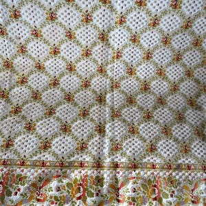 May include: Cream-colored textile with a diamond lattice pattern, adorned with small floral bouquets in shades of red, orange, and green. The bottom border features a detailed floral design with fringe. A vintage-inspired textile.
