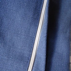 May include: Close-up of a dark blue fabric with a zipper running down the center. The zipper is white and has a slight sheen. The fabric is textured and has a subtle pattern.