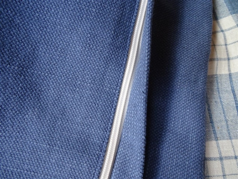 May include: Close-up of a dark blue fabric with a zipper running down the center. The zipper is white and has a slight sheen. The fabric is textured and has a subtle pattern.