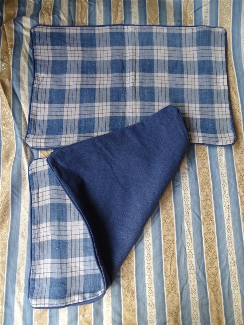 May include: Two blue and white plaid pillow covers with a dark blue border. The pillow covers are on a striped background.