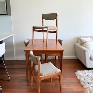 May include: A wooden dining table with four chairs. The chairs have a light-colored patterned fabric on the seat and back. The table and chairs are made of wood with a warm, natural finish. The room has hardwood floors.