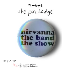 May include: A circular pin badge with the words "nirvanna the band the show" in rainbow hues. The badge has a holographic sheen. The text "n+bts the pin badge" is written above the pin badge.