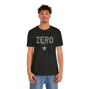 May include: Dark gray t-shirt with the word "ZERO" in light gray block letters, with "f*cks given" below and a star graphic. The shirt is a crew neck and short-sleeved.