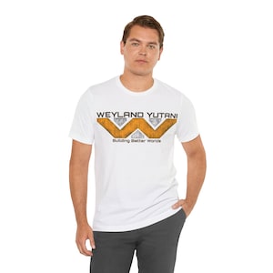 Può includere: T-shirt bianca con la scritta "WEYLAND YUTANI" sopra un logo stilizzato arancione e grigio, con lo slogan "Building Better Worlds" sotto. La maglietta è a girocollo.