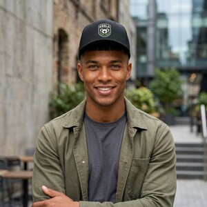 Puede incluir: Gorra de béisbol negra con el logo de Koala. La gorra tiene una visera curva y un ajuste estructurado. El logo presenta un koala y la palabra "KOALA" en blanco. La persona lleva una chaqueta verde y una camiseta gris.