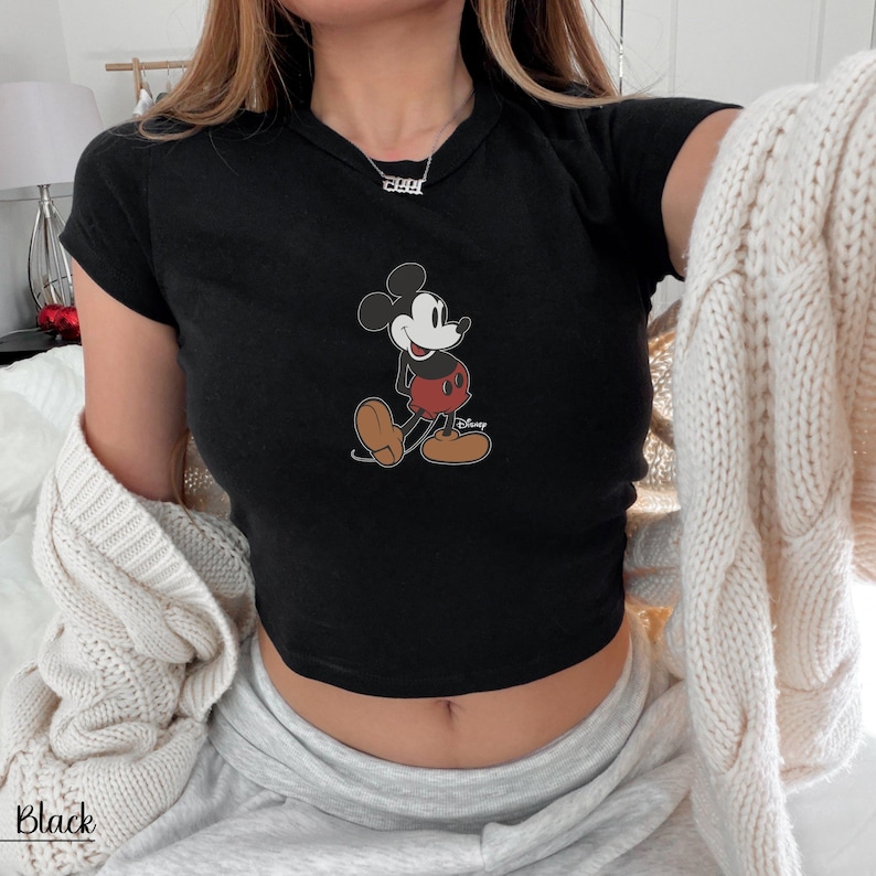 K&ouml;nnte beinhalten: Schwarzes Crop-Top mit Mickey Mouse-Grafik. Die Zeichentrickfigur tr&auml;gt rote Shorts, gelbe Schuhe und wei&szlig;e Handschuhe. Das Wort "Black" ist unten links im Bild aufgedruckt.