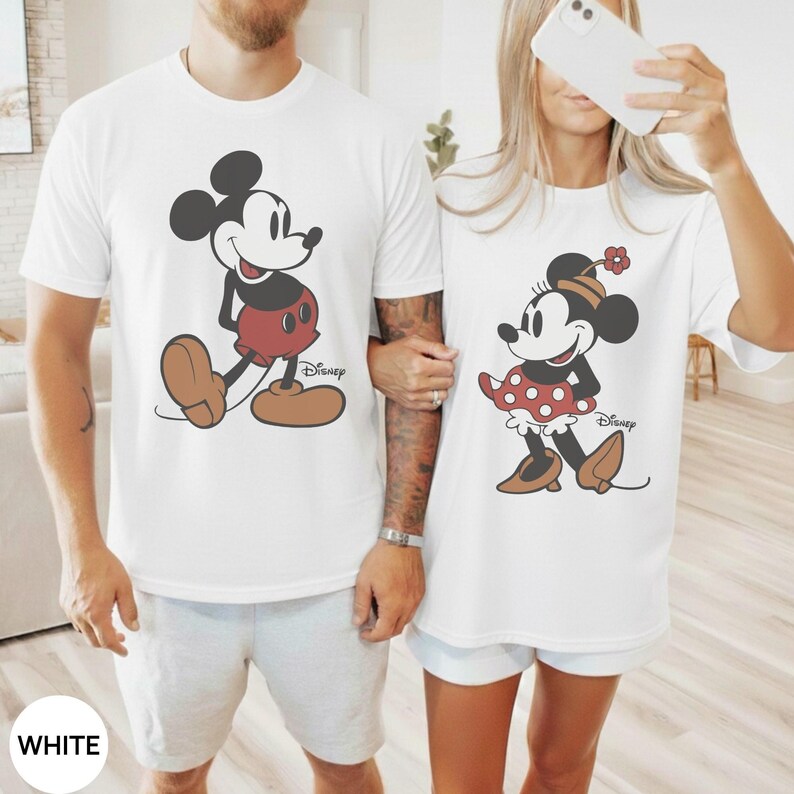 May include: White t-shirts featuring Mickey and Minnie Mouse. Mickey is in his classic outfit, and Minnie is in a polka-dot skirt. Both shirts have the Disney logo. The word "WHITE" is at the bottom of the image.