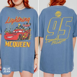 May include: Blue jean t-shirt featuring Lightning McQueen from the Cars movie. The front graphic shows McQueen with the text "Lightning 95 McQueen". The back of the shirt displays a large "95" and "Lightning McQueen" in yellow.