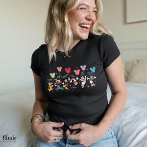 May include: Black t-shirt featuring a colorful graphic of Disney characters holding Mickey Mouse-shaped balloons. The characters include Pluto, Goofy, Mickey, Minnie, Daisy, and Donald Duck. The text "Happy Days" is also included.