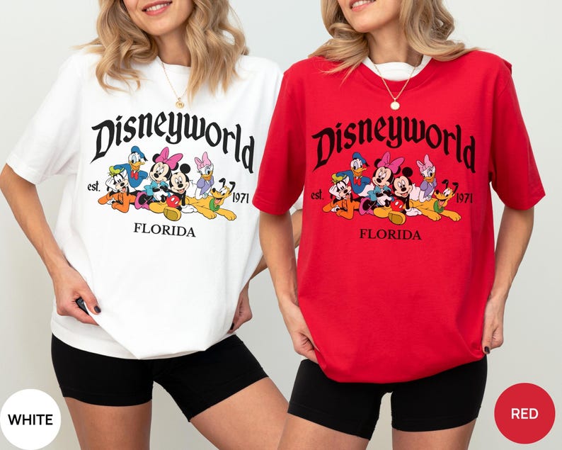 May include: A white t-shirt and a red t-shirt, each featuring a graphic print with the text Disneyworld, est. 1971, and FLORIDA. The design includes illustrations of Mickey Mouse, Minnie Mouse, Donald Duck, Daisy Duck, Goofy, and Pluto.