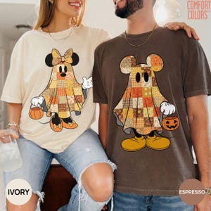 May include: Two short-sleeve crew neck t-shirts, one ivory and one espresso, each featuring a graphic of a ghost wearing a patchwork-patterned sheet and holding a jack-o'-lantern bucket. The ghost on the ivory shirt wears a bow.