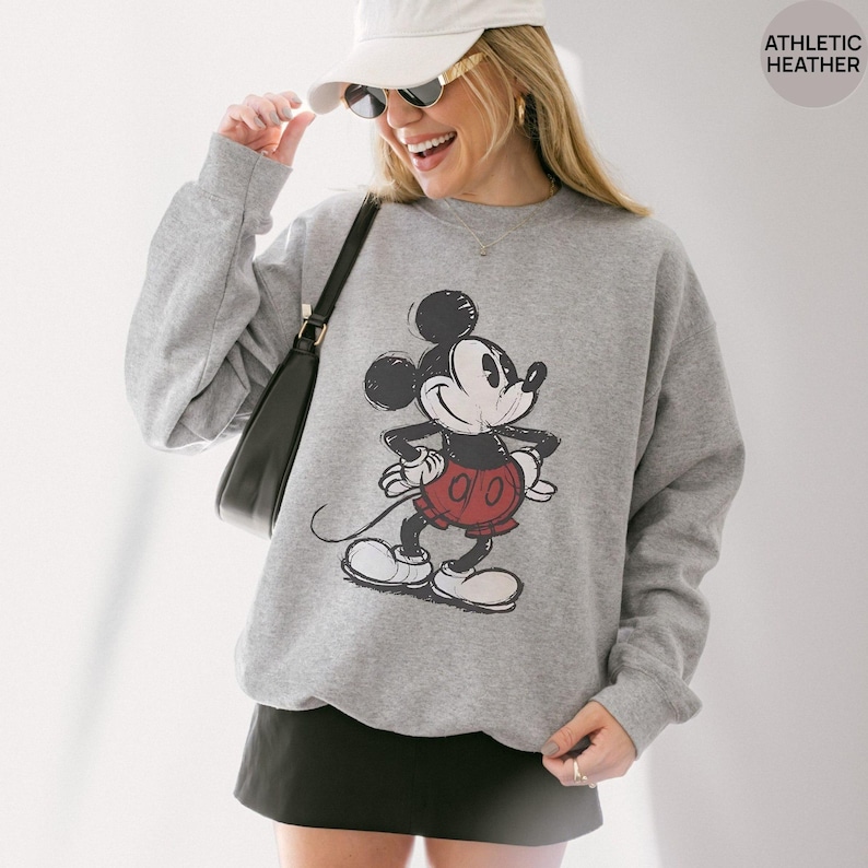 May include: Athletic heather gray sweatshirt featuring a distressed graphic of Mickey Mouse in black, red, and white. The sweatshirt has a crew neck and long sleeves. The text "ATHLETIC HEATHER" is in the upper right corner.