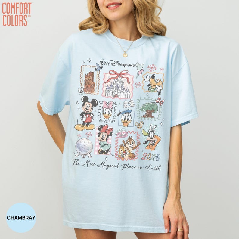 May include: A light blue short-sleeve t-shirt featuring a graphic print with the text "Walt Disneyland" and "The Most Magical Place on Earth" along with illustrations of Mickey Mouse, Minnie Mouse, Donald Duck, Goofy, and the year 2026.