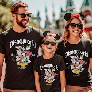 May include: Three black t-shirts featuring the white text Disneyworld, est. 1971, and FLORIDA. The graphic includes colorful illustrations of Mickey Mouse, Minnie Mouse, Donald Duck, Daisy Duck, Goofy, and Pluto. The shirts have a crew neckline.
