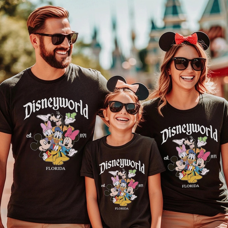 May include: Three black t-shirts featuring the white text Disneyworld, est. 1971, and FLORIDA. The graphic includes colorful illustrations of Mickey Mouse, Minnie Mouse, Donald Duck, Daisy Duck, Goofy, and Pluto. The shirts have a crew neckline.