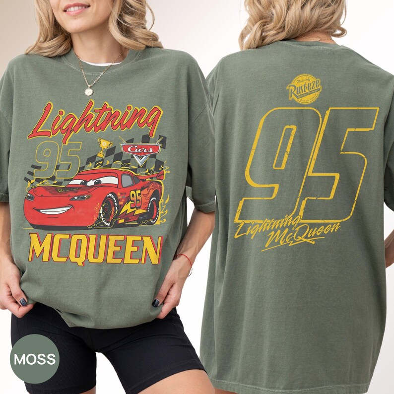May include: Moss green t-shirt featuring Lightning McQueen from the Cars movie. The front graphic includes the text "Lightning 95 McQueen" with a red race car. The back displays a large yellow "95" and "Lightning McQueen".